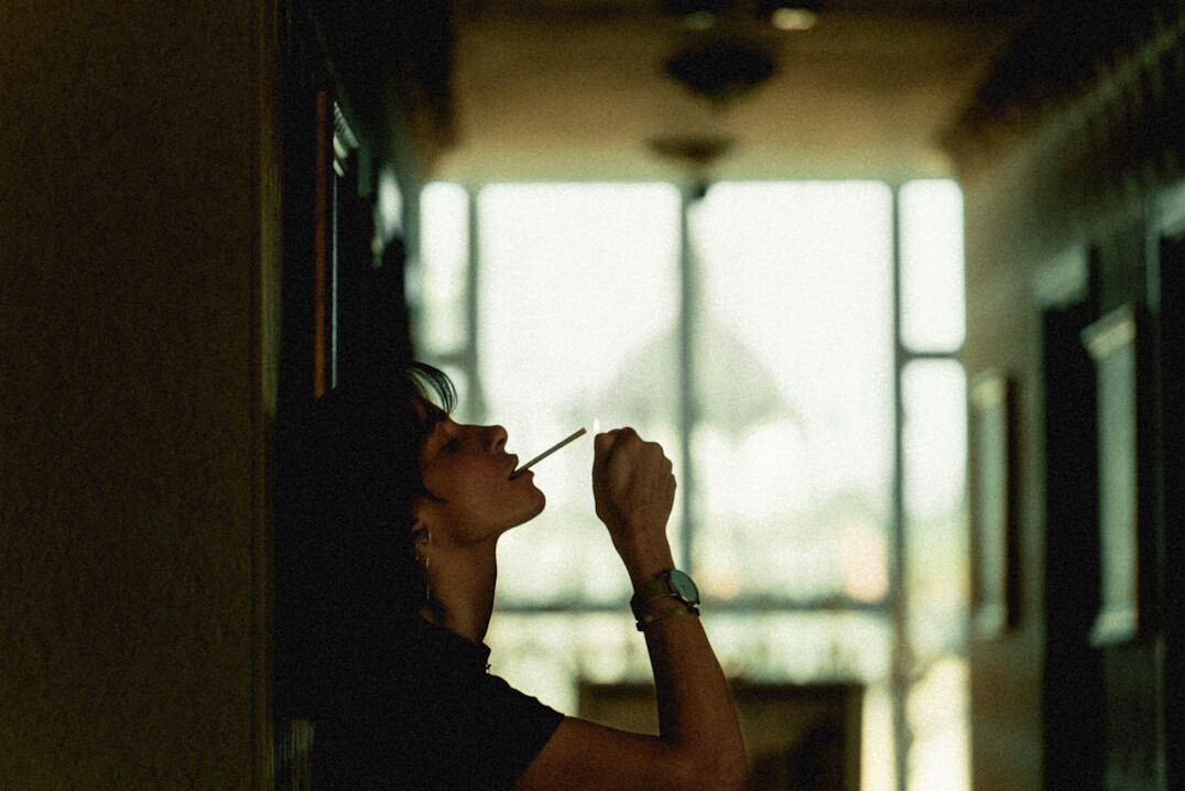 Person writing thoughtfully in a journal near a window